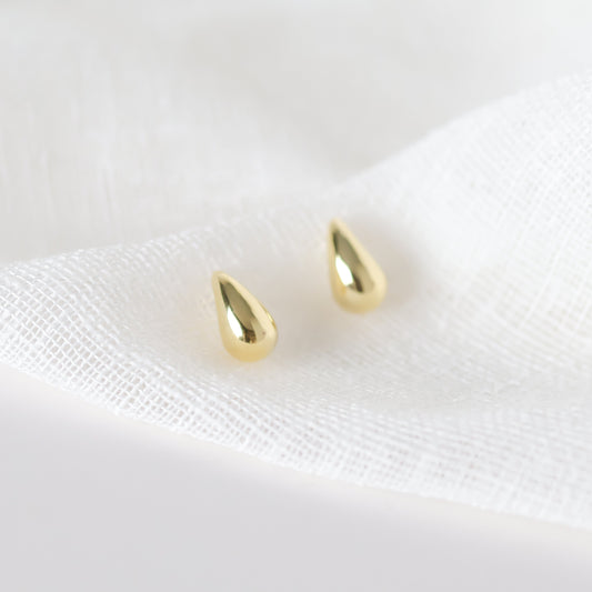 A pair of gold tapered huggie hoop earrings on a white background.