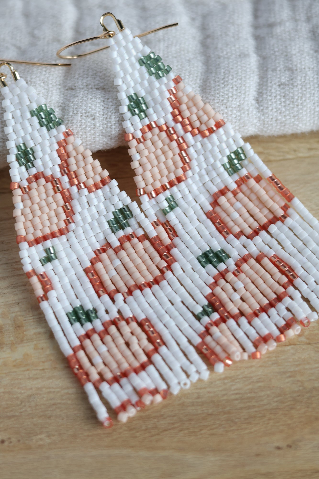 A pair of peach-shaped shakers with white, peach, and green beads, displayed on a wooden surface.