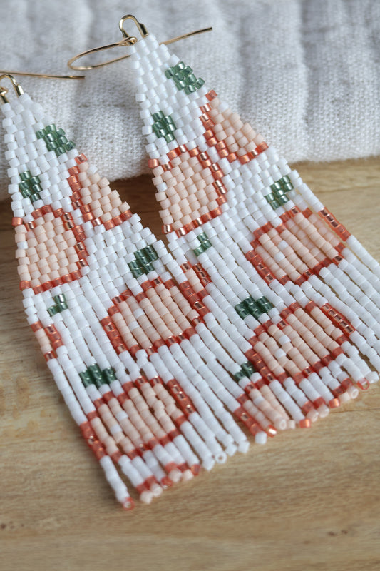 A pair of peach-shaped shakers with white, peach, and green beads, displayed on a wooden surface.