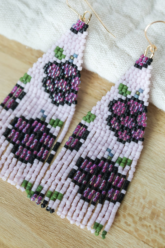 A pair of beaded earrings designed in the shape of blackberries, predominantly purple with green accents, displayed against a neutral background.