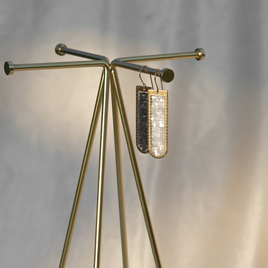 Gold tripod stand with a decorative handmade beaded earrings against a gray background