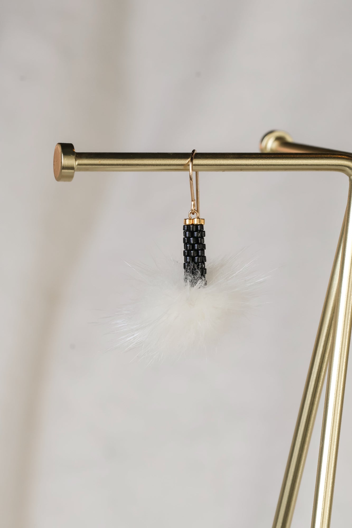 Gold earring with black beads hanging on a gold stand against a light background