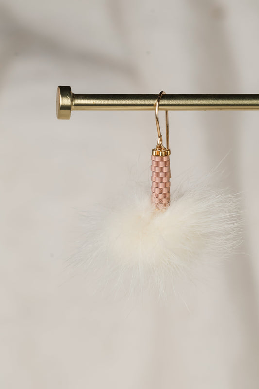 Pink beaded earrings hanging from a gold hook on a soft white background