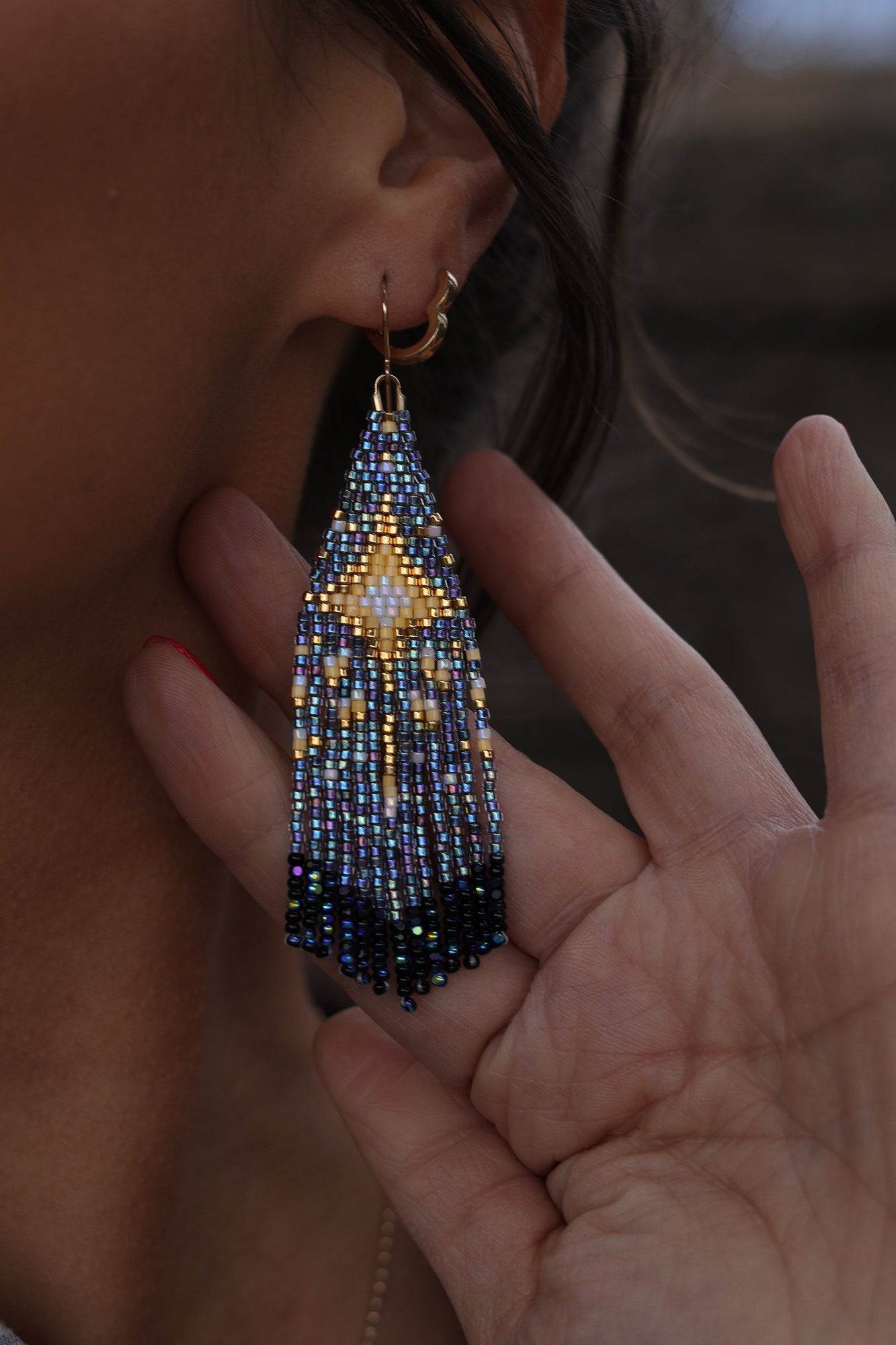 Close-up of a hand holding a beaded earring near an ear.