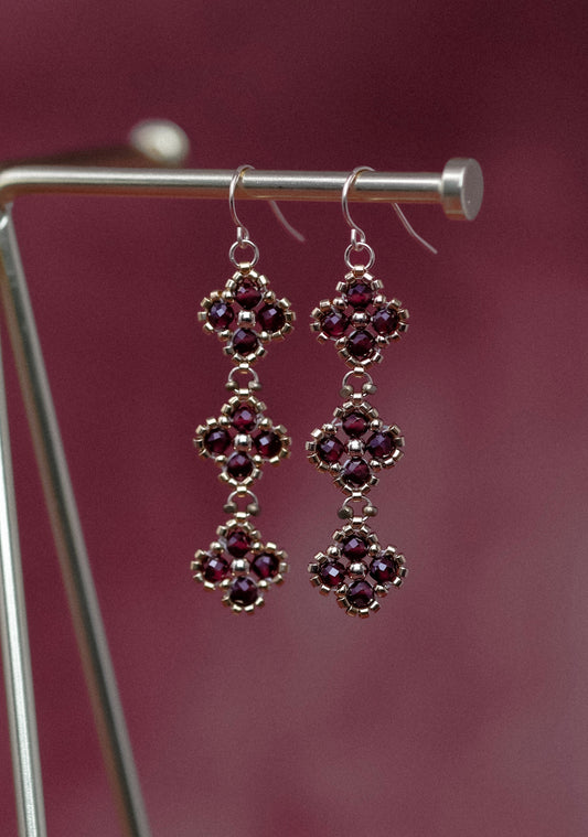 Pair of ornate beaded earrings on a stand against a maroon background