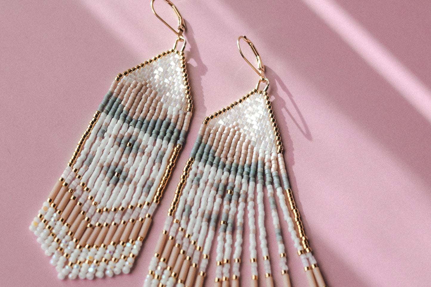 Beaded earrings with gold accents on a pink background