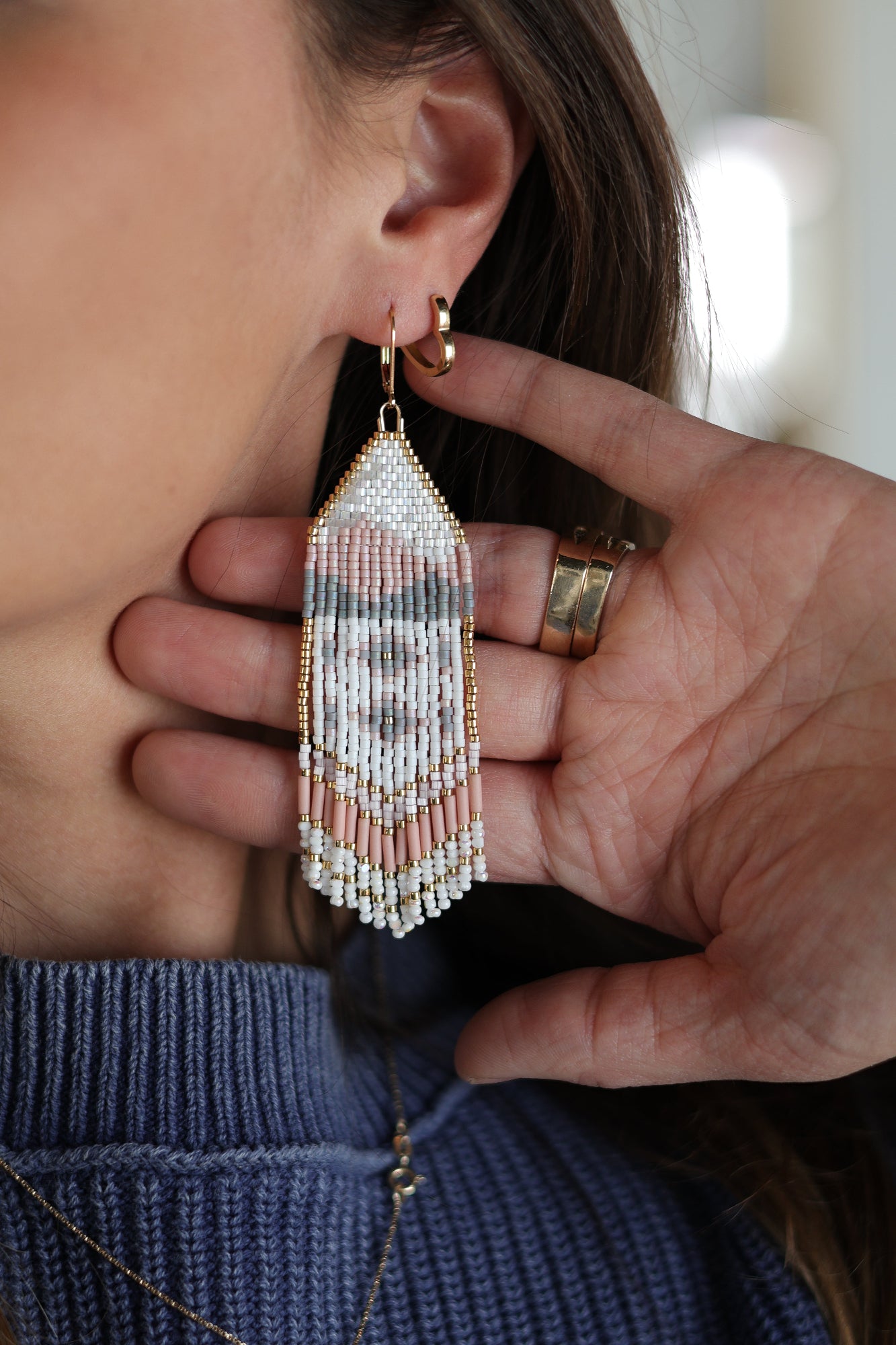 Person wearing a beaded earring with a hand adjusting it.