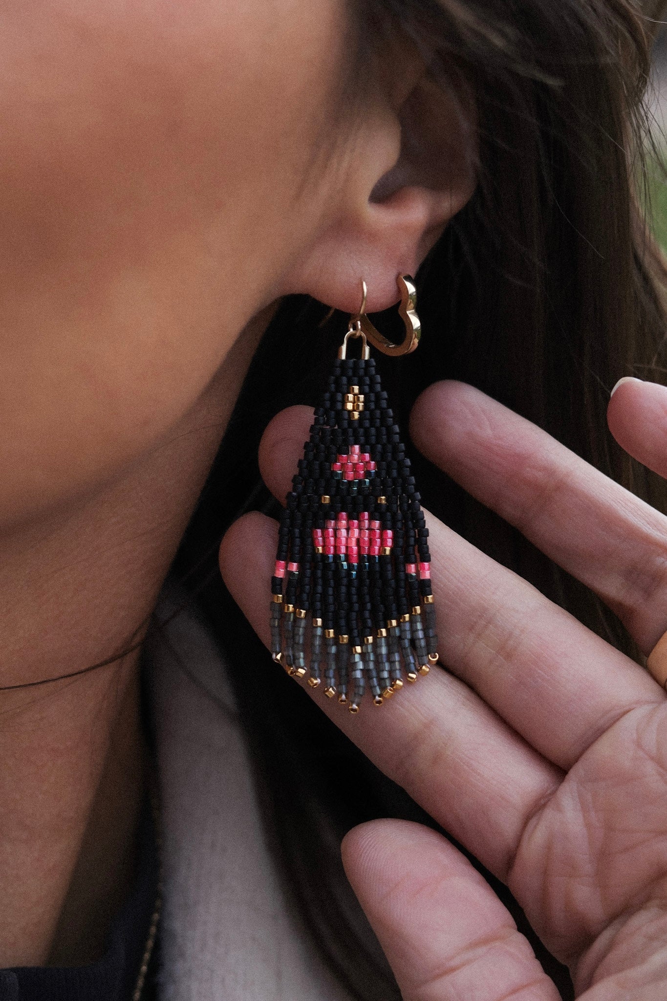 Close-up of a person wearing a beaded earring with intricate patterns.