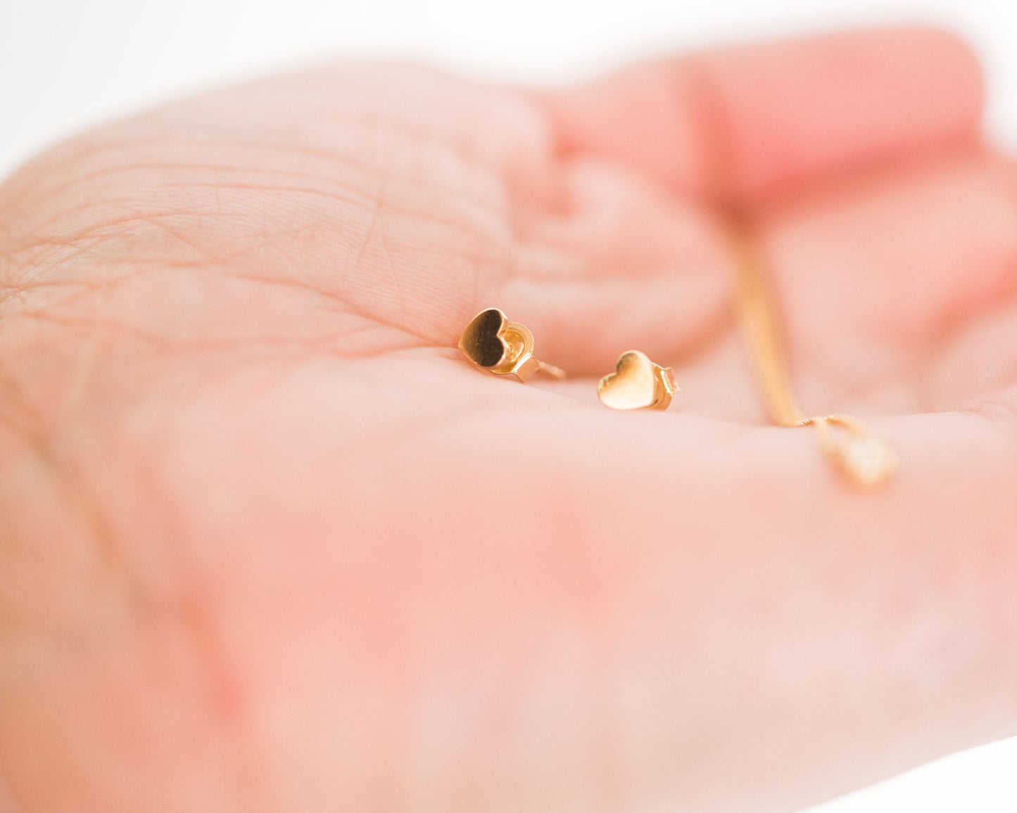 Gold heart-shaped earrings on a hand against a white background