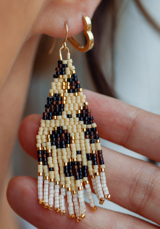 Beaded earrings held between fingers with a blurred background