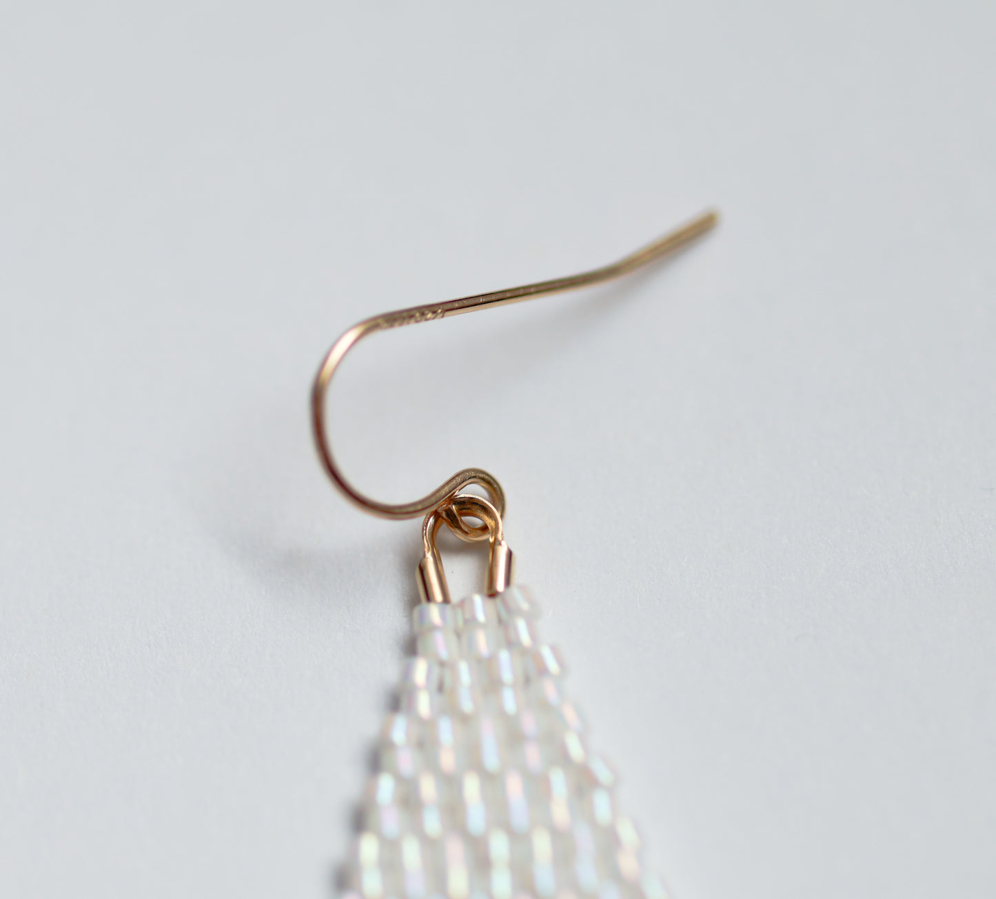 Handmade beaded earring with white beaded fringe on a light gray background