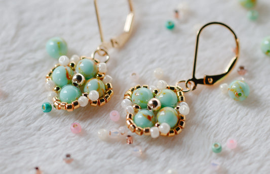 Pair of handmade beaded earrings with green and gold design on a light background