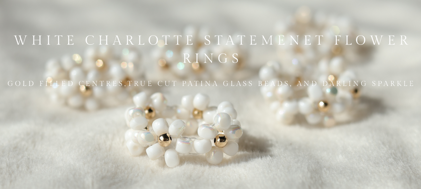 White Charlotte statement flower rings with gold accents on a light background