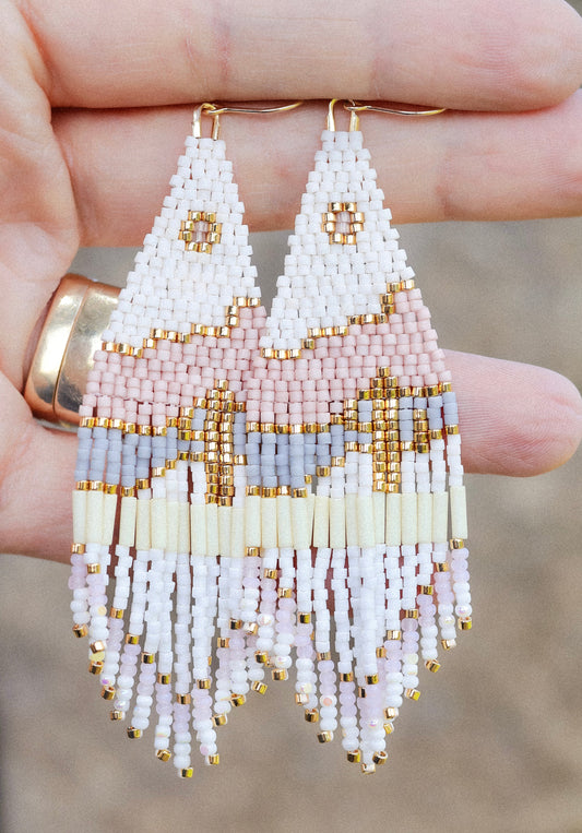 Beaded earrings held between fingers against a blurred background