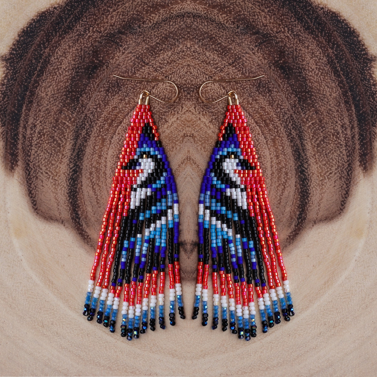 Triangular beaded earrings with red, blue, and black pattern on a textured brown background