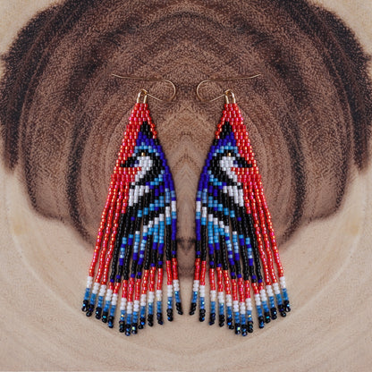 Triangular beaded earrings with red, blue, and black pattern on a textured brown background