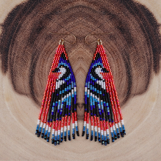 Triangular beaded earrings with red, blue, and black pattern on a textured brown background