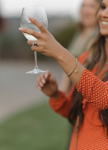 Woman wearing a gold bracelet with a heart pendant while toasting with a wine glass