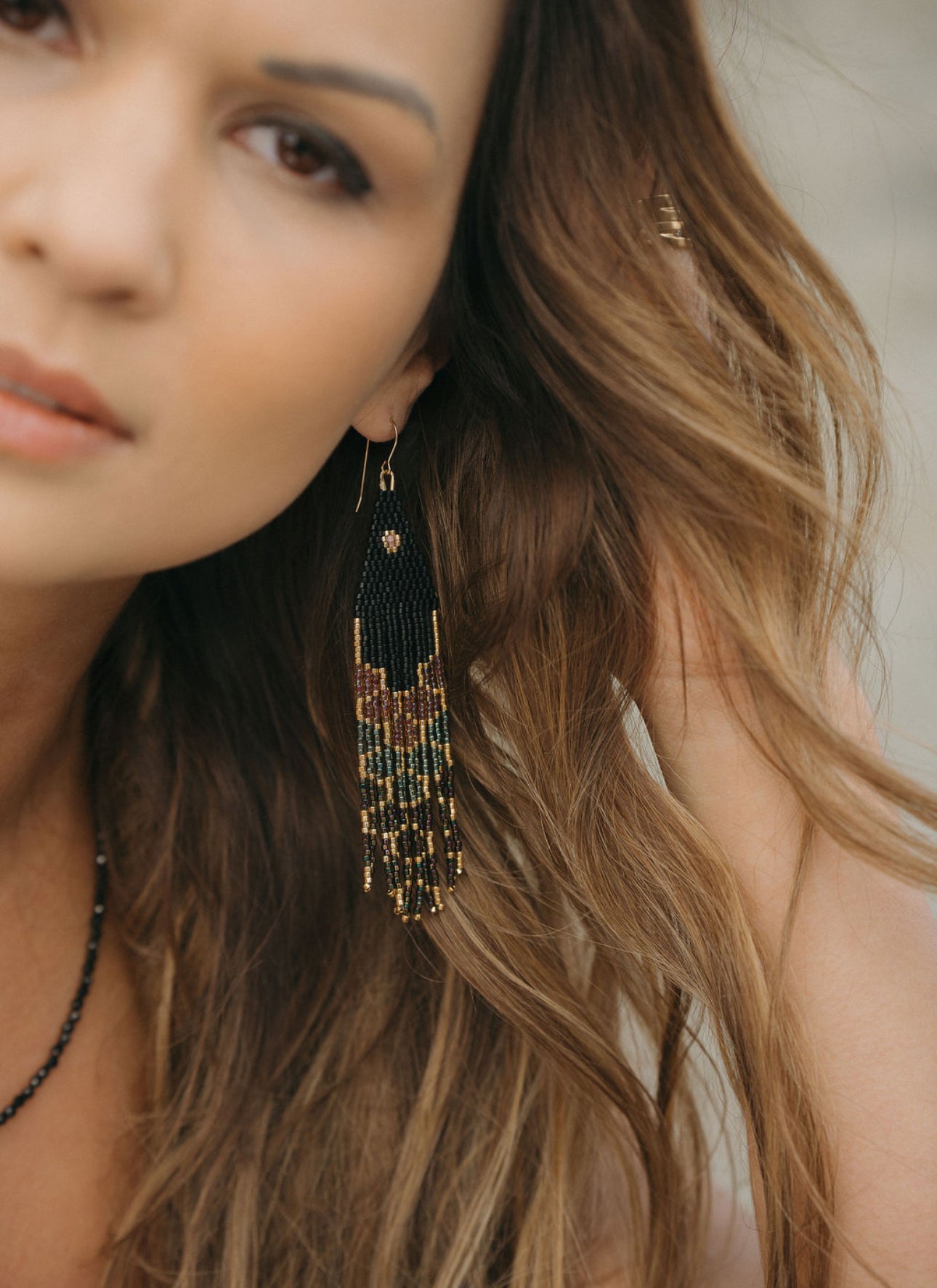 Close-up of a woman wearing intricate, handmade beaded earrings with a neutral background