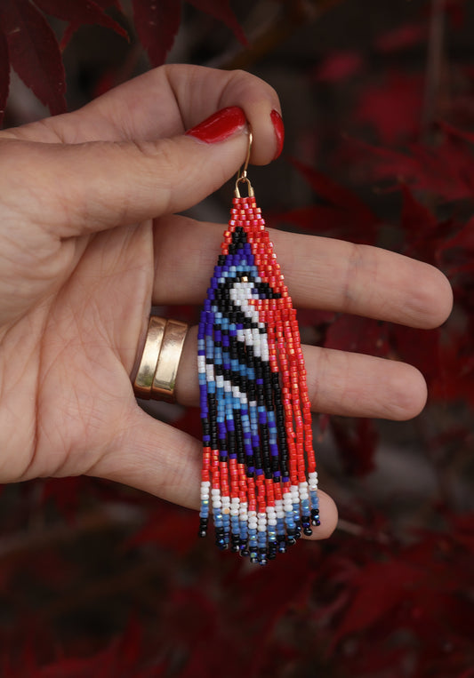 Hand holding a beaded earring with a colorful pattern against a blurred red background