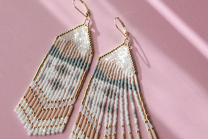 Beaded earrings with gold accents on a pink background