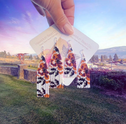 Handmade beaded earrings held up with a scenic background