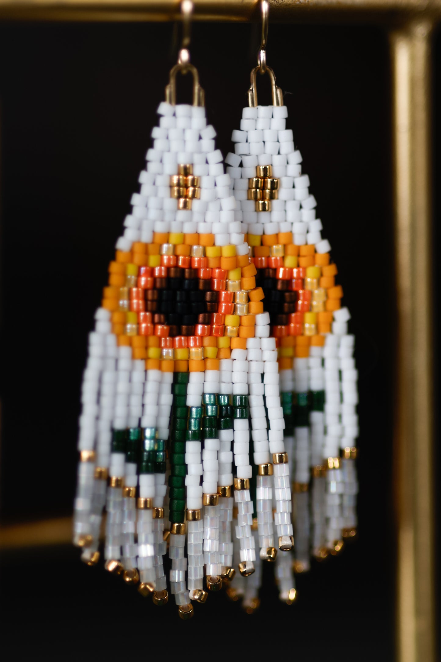 Beaded earrings with white, orange, and green design on a dark background