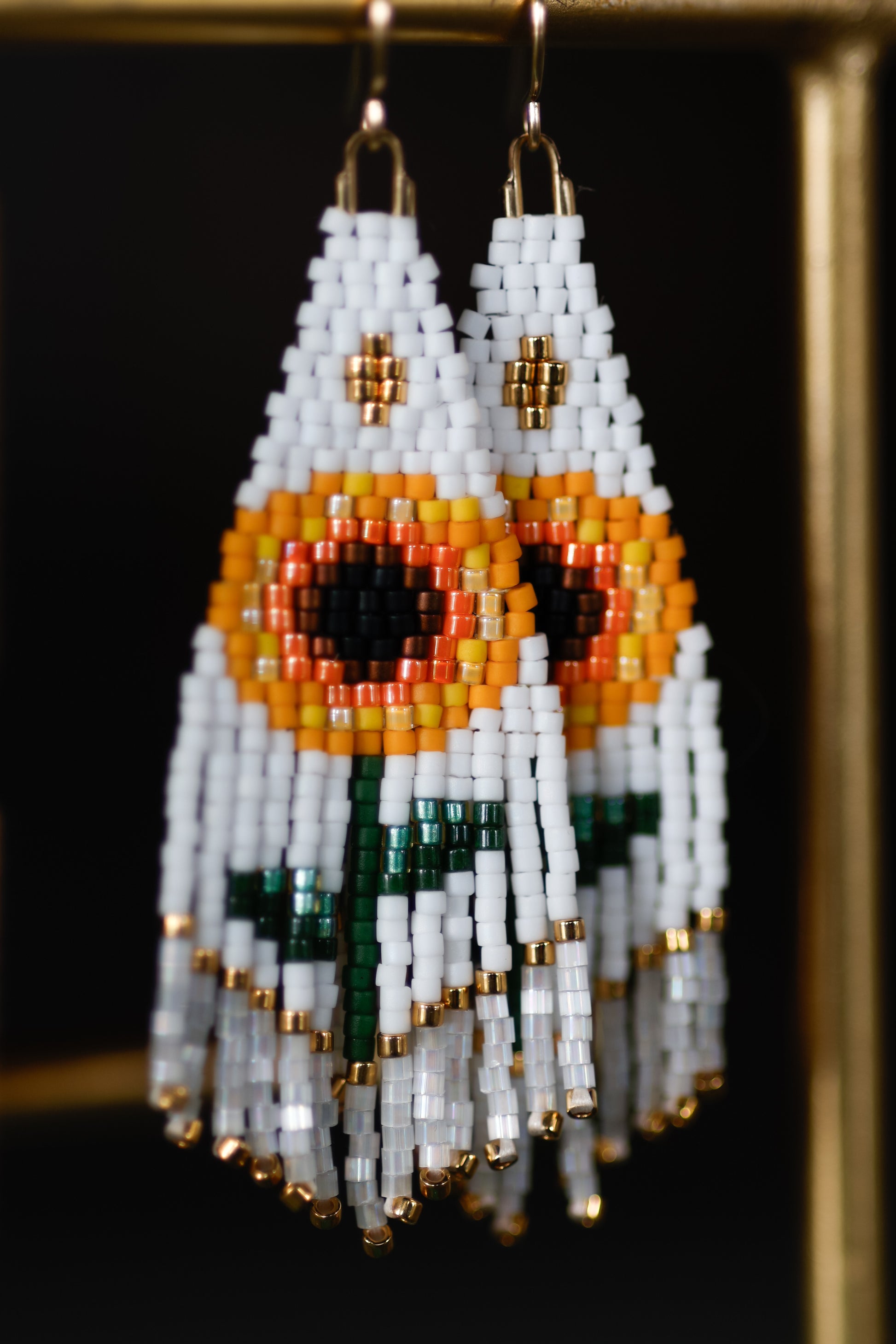 Beaded earrings with white, orange, and green design on a dark background