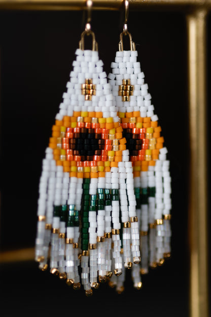Beaded earrings with white, orange, and green design on a dark background