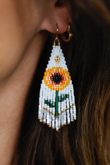 Close-up of a beaded earring with a sunflower design worn by a person.
