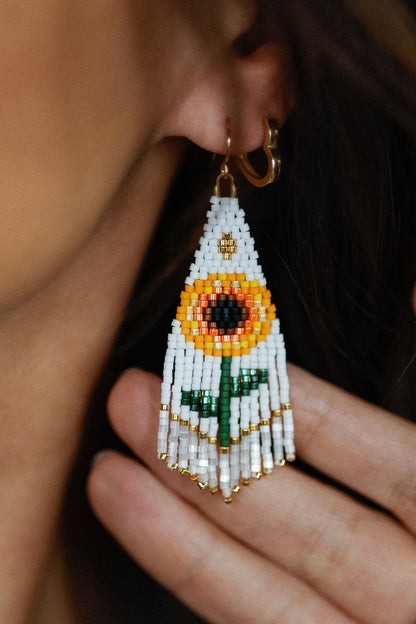 Close-up of a beaded sunflower earring worn by a person.