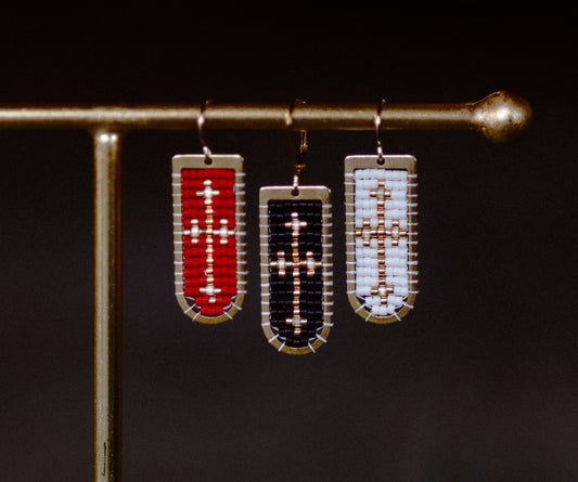 Three beaded earrings on a stand against a dark background
