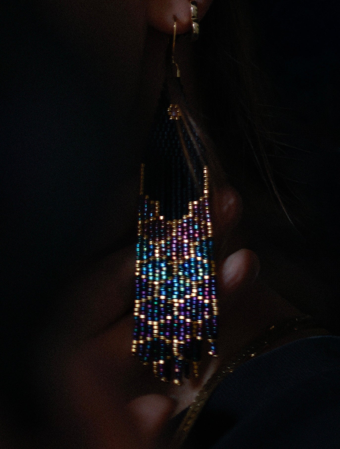 Handmade beaded earrings held by a hand against a dark background