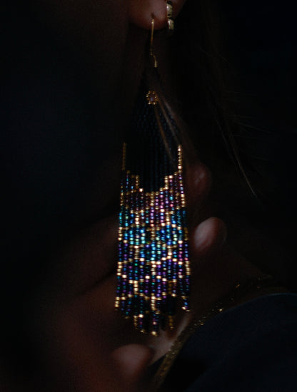 Handmade beaded earrings held by a hand against a dark background