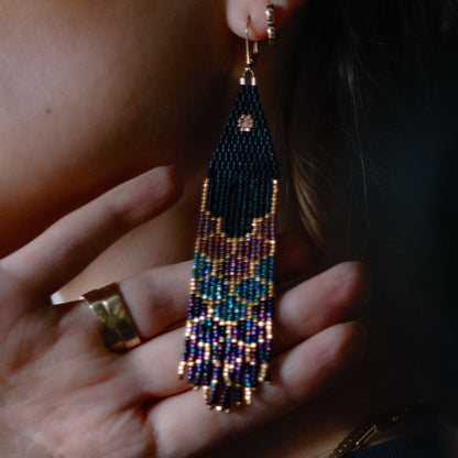 Close-up of a hand holding a beaded earring with intricate design.