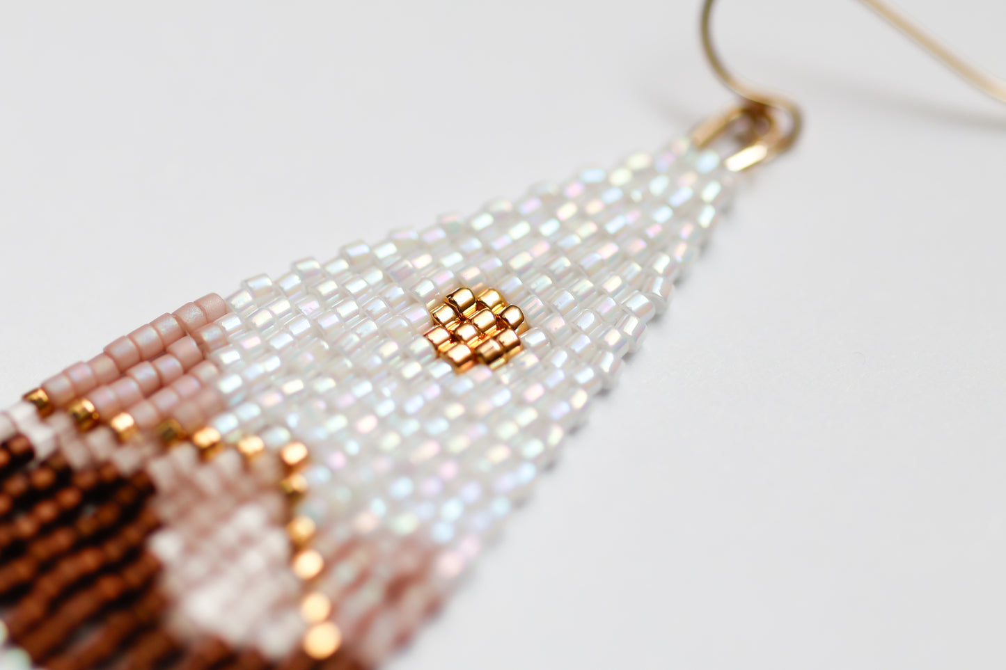 Close-up of handmade beaded earrings with white, gold, and brown beads on a light background