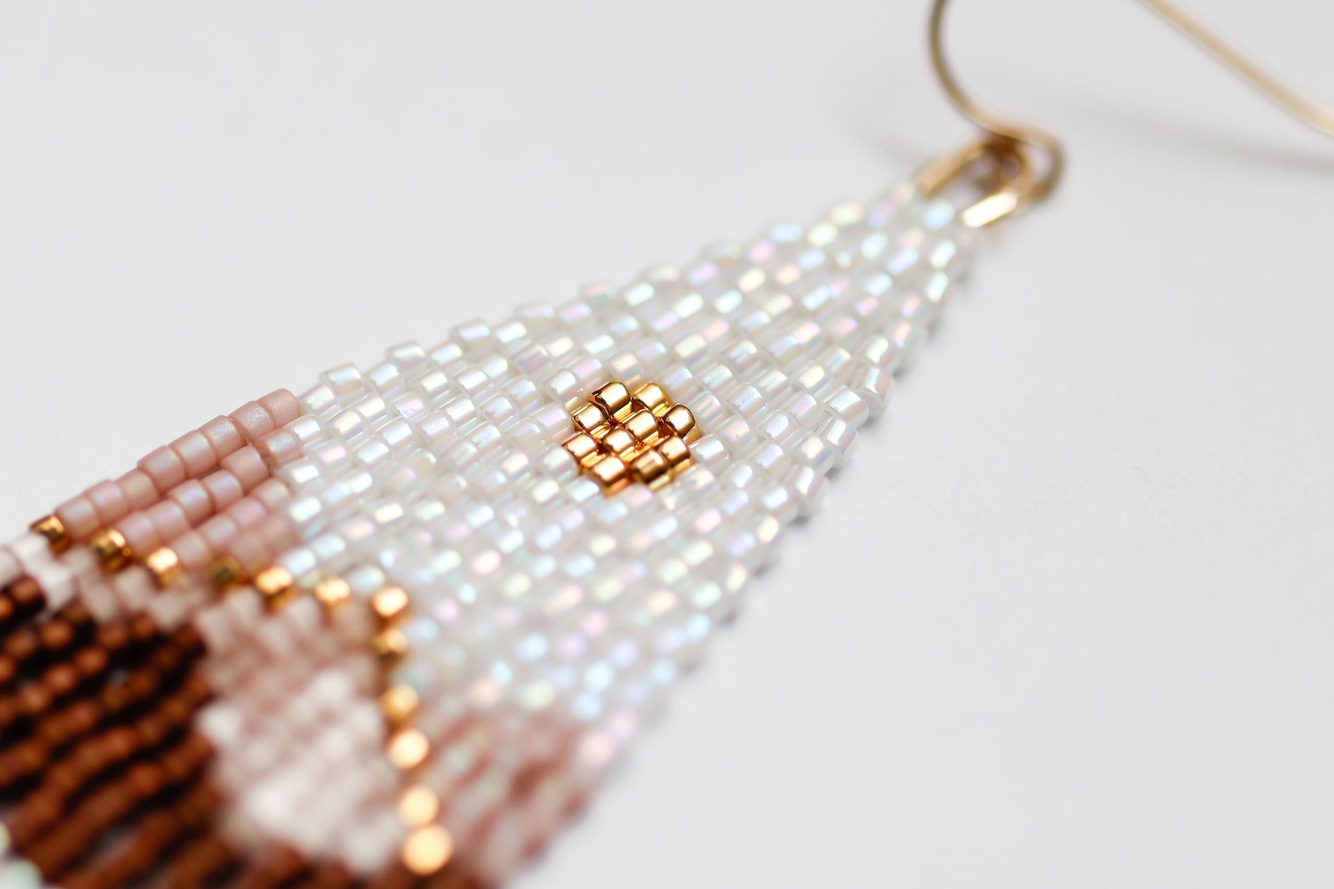 Close-up of handmade beaded earrings with white, gold, and brown beads on a light background