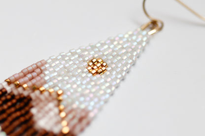 Close-up of handmade beaded earrings with white, gold, and brown beads on a light background