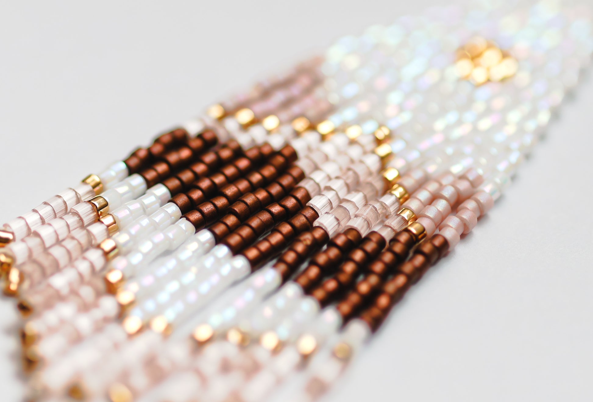 Close-up of handmade beaded earrings in white, brown, and gold on a light background