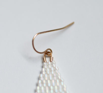 Handmade beaded earring with white beaded fringe on a light gray background