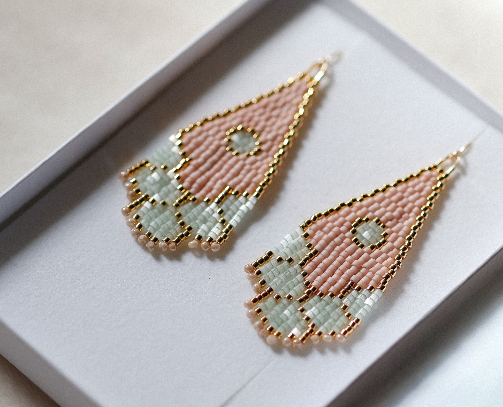 Pair of geometric handmade beaded earrings with pink and gold design on a white background