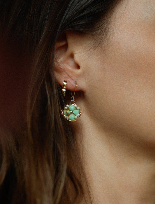 Close-up of an ear wearing a handmade  beaded turquoise earring with gold accents.