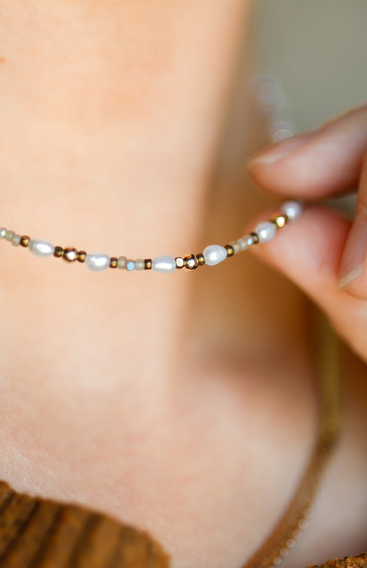 Close-up of a delicate beaded necklace being held against a blurred background