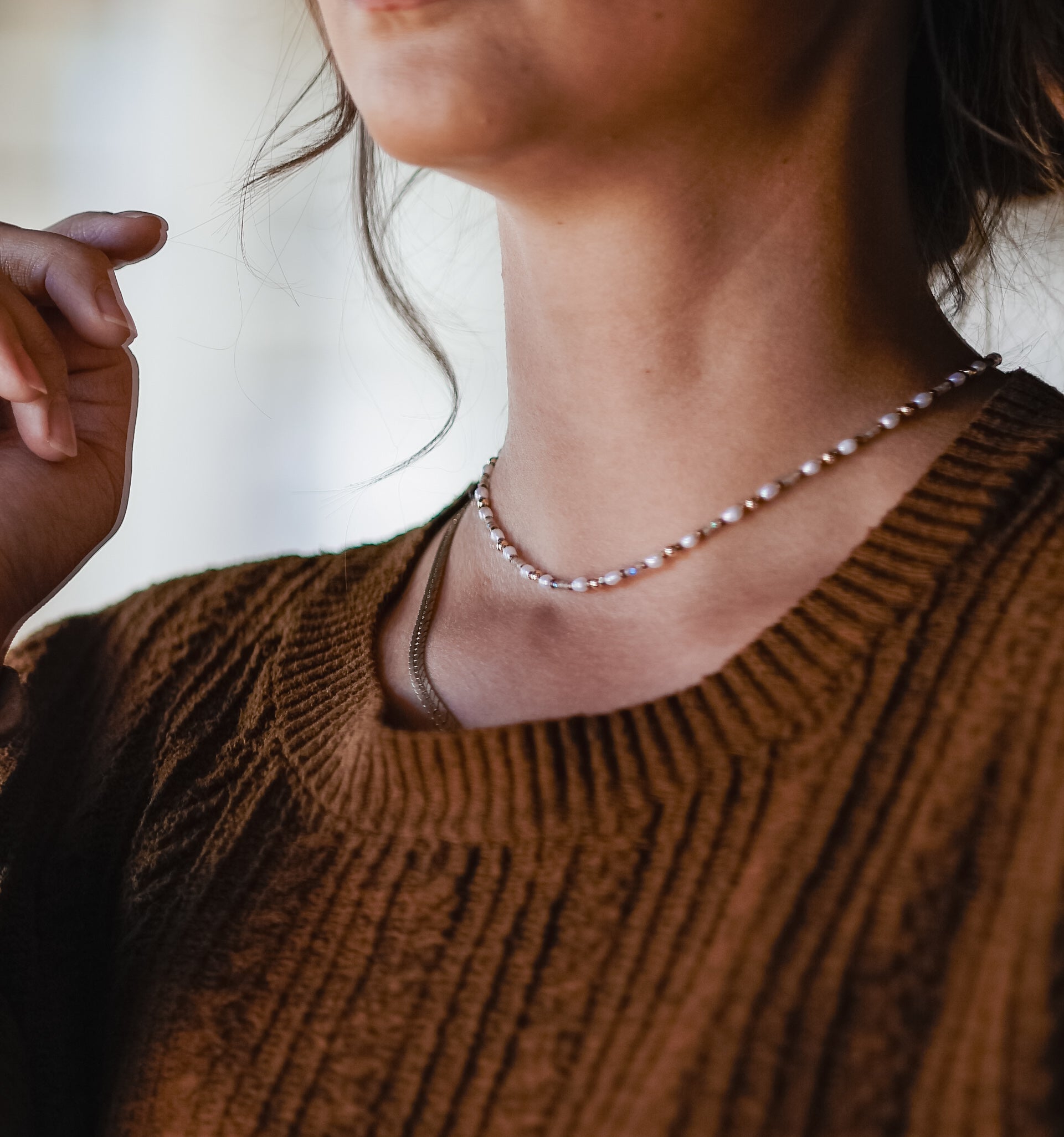 Woman in a brown sweater wearing a dainty beaded necklace