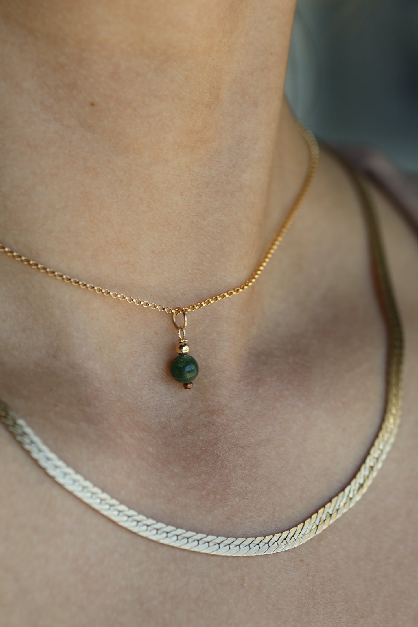 Gold necklace with a green gemstone pendant on a person's neck