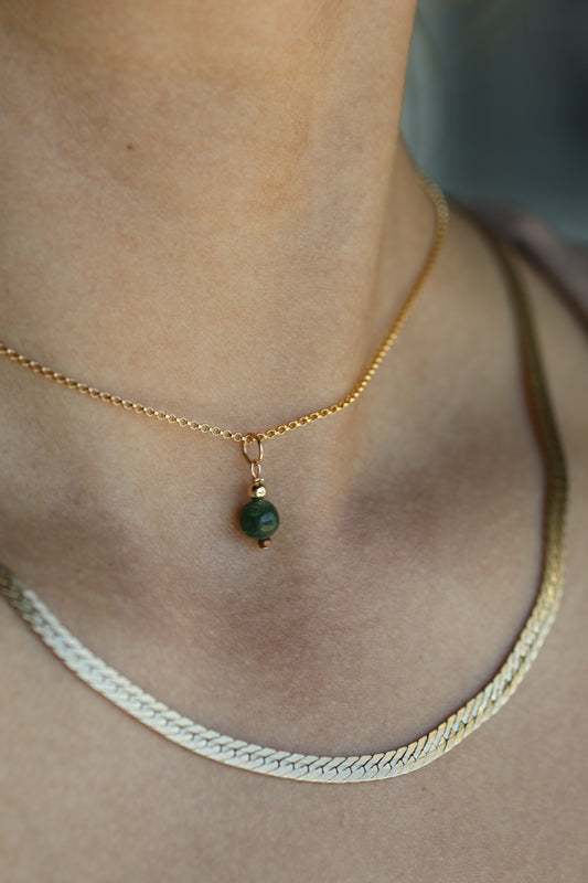 Gold necklace with a green gemstone pendant on a person's neck