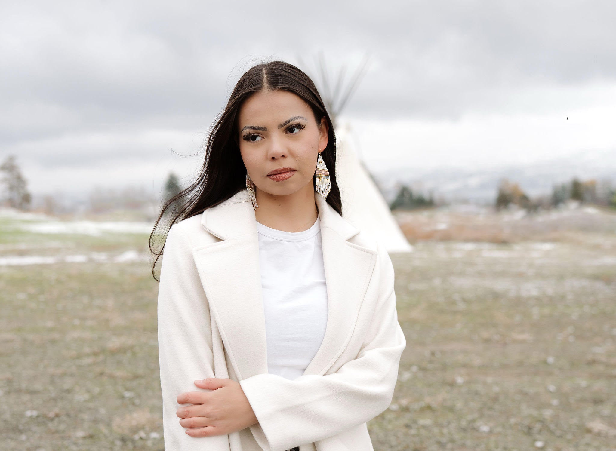 Woman in a white coat standing in a field with a cloudy sky